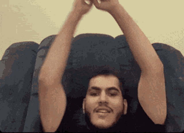a man with a beard is sitting on a couch with his arms in the air