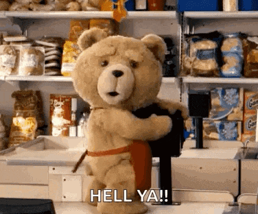 a teddy bear wearing an apron is standing in a store and holding a black object .