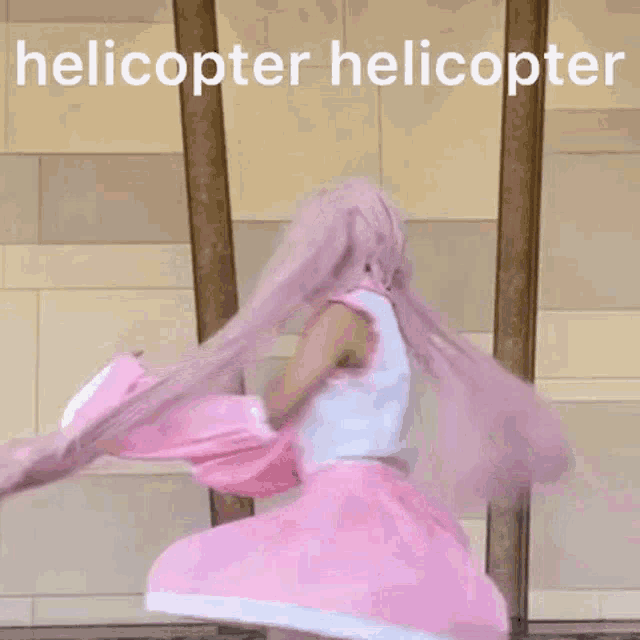 a woman in a pink wig is standing in front of a wall with the words helicopter helicopter written above her .