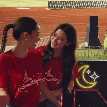 two women wearing red lena mia shirts are hugging and smiling