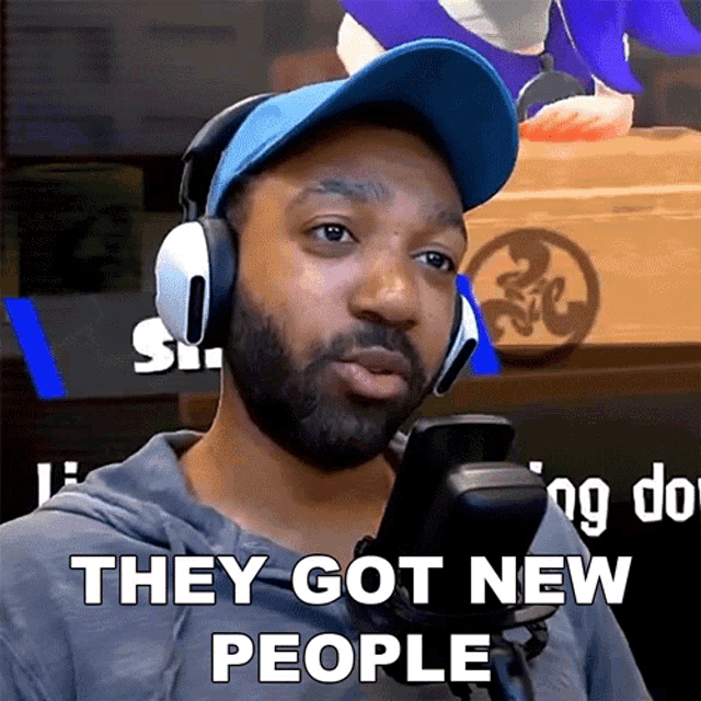a man wearing headphones and a blue hat says " they got new people "