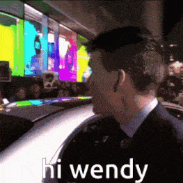 a man in a suit and tie is standing in front of a car with the words hi wendy written on it .