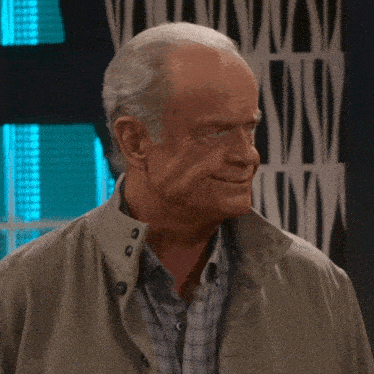 a man wearing a jacket and plaid shirt stands in front of a wall that has the letter n on it