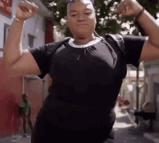 a woman in a black dress is flexing her muscles while standing on a street .