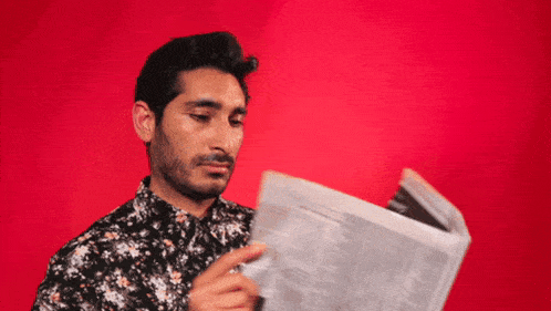 a man in a floral shirt is reading a newspaper on a red background