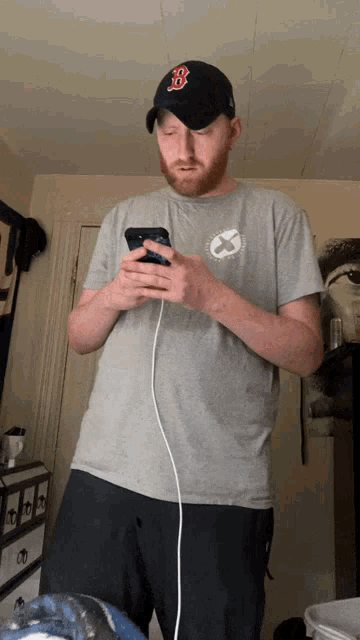 a man wearing a boston red sox hat is looking at his phone