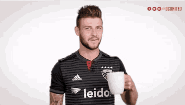 a man wearing a leidos shirt is holding a cup