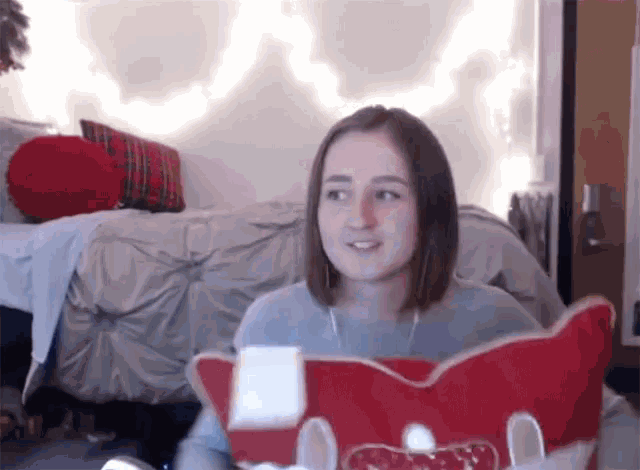 a girl sitting in front of a bed with a red pillow