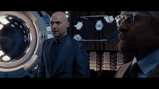 a bald man in a blue suit and tie is standing in front of a circular screen
