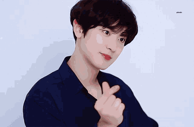 a young man in a blue shirt is making a heart shape with his hands
