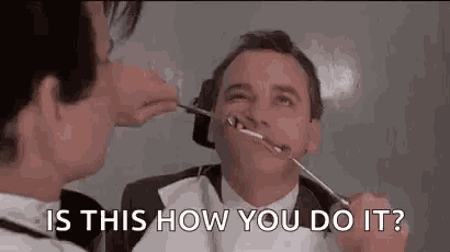 a man is getting his teeth examined by a dentist while another man looks on .