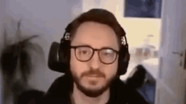 a man with a beard wearing headphones and glasses is looking at the camera .