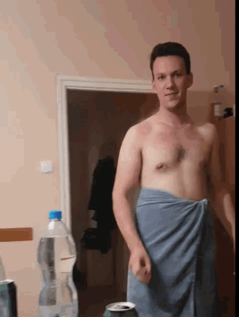 a shirtless man wrapped in a blue towel is standing in front of a bottle of water