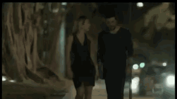 a man and a woman are walking down a street at night .