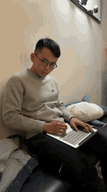 a man wearing glasses and a grey nike sweater is typing on a laptop