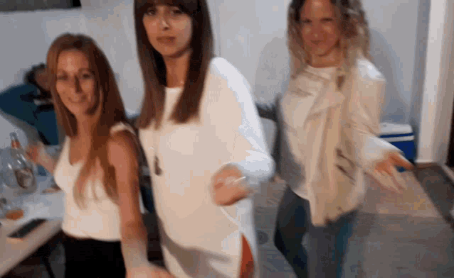 three women are dancing in a room and one is wearing a white shirt