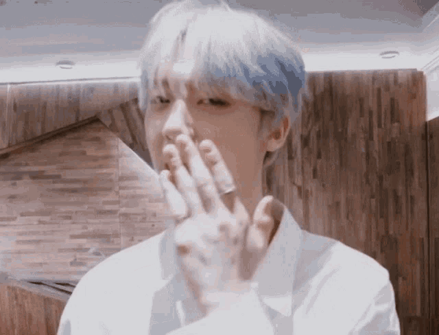 a man with blue hair is covering his mouth with his hand