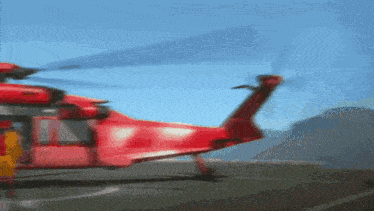 a red helicopter is landing on a runway