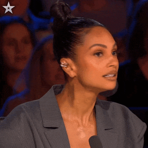 a woman wearing a gray jacket and ear cuffs is talking into a microphone .