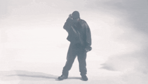 a man in a black jacket is standing in front of a white wall .