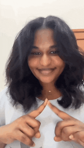 a woman is smiling and making a heart with her fingers