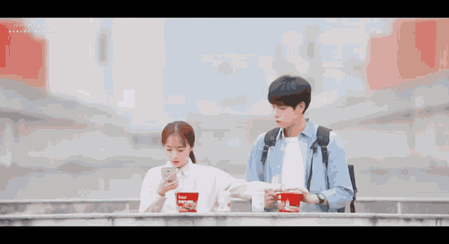 a girl is looking at her phone while a boy holds a bowl of beef noodle
