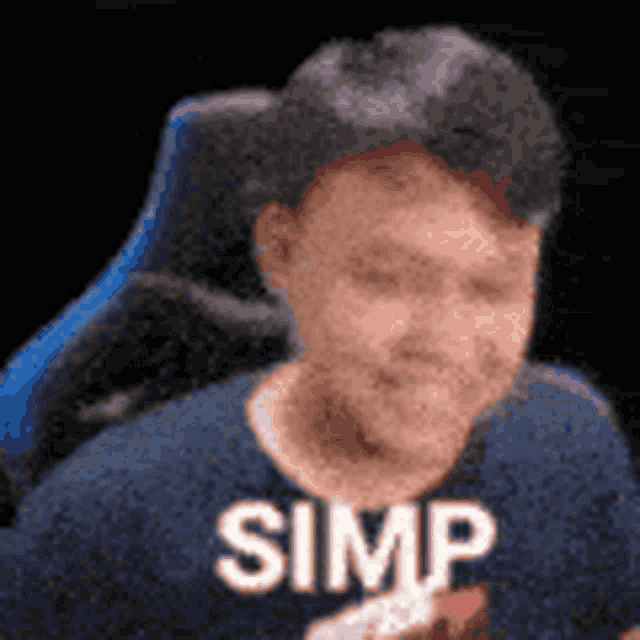 a man in a blue shirt is sitting in a chair with the word simp written on his chest .