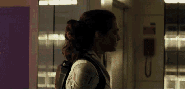 a woman in a white suit is walking down a hallway with a phone on the wall