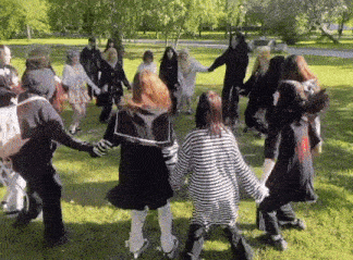 a group of people are holding hands in a circle in the grass .