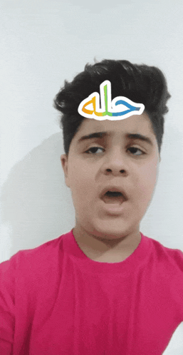 a boy wearing a pink shirt has a sticker on his head that says allah