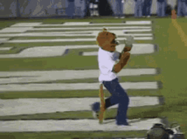 a mascot is running on a football field wearing a white shirt and blue jeans .