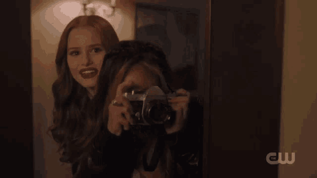a woman is taking a picture of another woman with a camera with cw written on the bottom