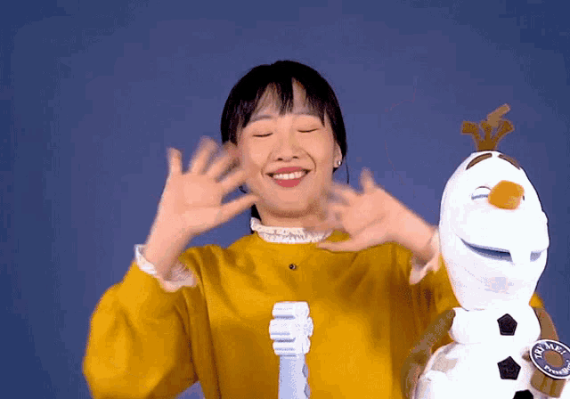 a woman in a yellow shirt is holding a stuffed snowman and a toothbrush that says ' olaf ' on it