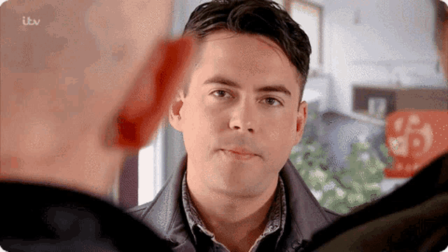 a man in a leather jacket talks to another man with itv written on the bottom right