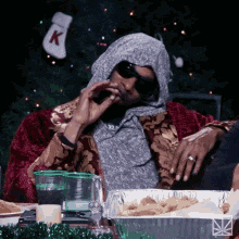 a man is sitting at a table with a christmas tree in the background and a christmas stocking with the letter k on it