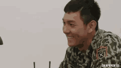a man in a military uniform is smiling while sitting in front of a white wall .