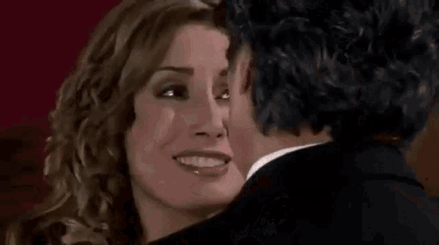 a man and a woman are kissing in a room . the man is wearing a suit and tie .