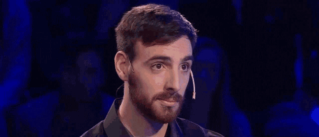 a man with a beard is wearing a microphone in front of a crowd of people .