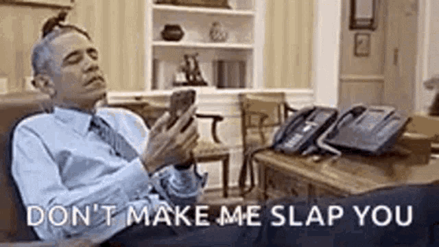 a man in a suit and tie is sitting in a chair looking at his cell phone .