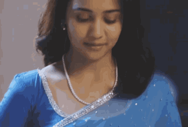 a woman wearing a blue blouse and a pearl necklace looks down