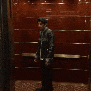 a man in a leather jacket is standing in a dark room