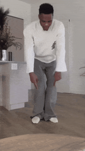 a man in a white shirt and grey pants is standing on a wooden floor