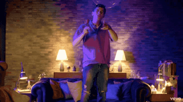 a man in a red shirt is standing in front of a couch with vevo written on the bottom of the screen