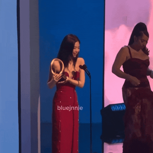 a woman in a red dress stands in front of a microphone with the name bluejinnie written on the bottom
