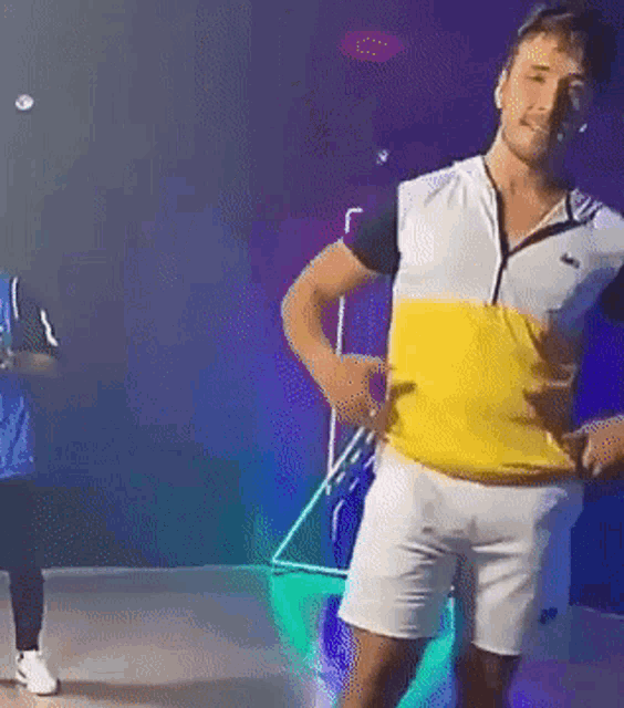a man in a yellow and white shirt and white shorts is dancing in a dark room .