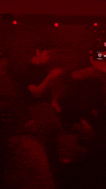 a man is taking a picture of a group of people in a dark room with red lights .