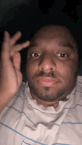 a man with a beard and a white shirt is making a funny face with his hand .