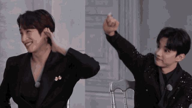 two men in black suits are sitting next to each other and one is pointing
