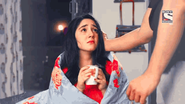 a woman is wrapped in a blanket and holding a cup of coffee while a man holds her head .