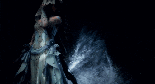 a woman in a white dress is standing in front of a waterfall